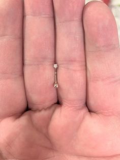 a person's hand holding a tiny diamond ring in their left hand with the middle finger