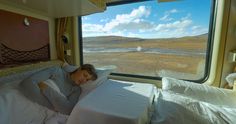 a woman laying in bed next to a window with the view of an open field