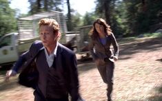 two people are running in the woods with one person wearing a suit and another walking behind them