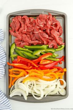 an assortment of vegetables including peppers and meat in a baking pan on a white table