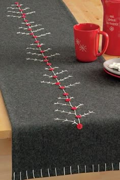 a table topped with two red mugs next to a black table runner covered in pins