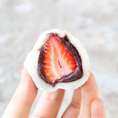 a person holding up a small pastry with a strawberry on it