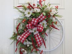 a wreath with red and white flowers hanging on a door