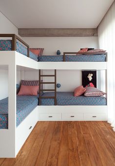 two bunk beds in a room with wooden floors and white walls, one is blue and the other has pink pillows