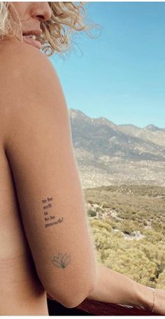 a woman with a small tattoo on her left arm and shoulder is looking out over the desert