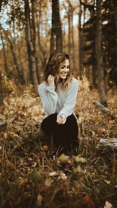 a woman is sitting in the woods with her hands on her hips and smiling at the camera