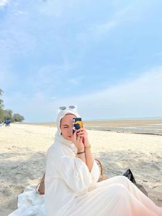 a woman sitting on the beach taking a photo with her cell phone