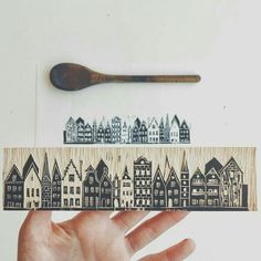 a hand holding a piece of wood with houses on it and a spoon in the background