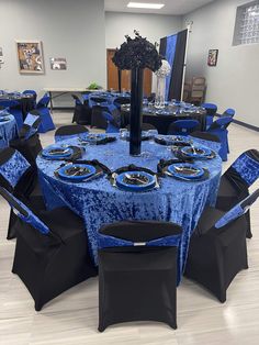 a blue table cloth with black chairs and plates on it is set up for an event