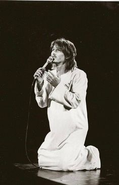 a man sitting on the ground while holding a microphone in his right hand and singing into a mic