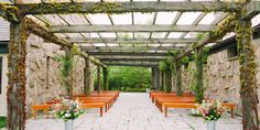 an outdoor wedding venue with orange benches and flowers on the aisle, surrounded by stone walls