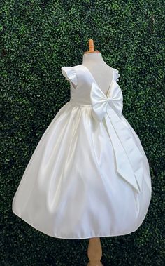 Our enchanting Ankle Length flower girl dresses are sure to turn heads! This beautiful elegant sophisticated dress is handmade, the bodice consists of Ivory Bridal Satin with a sowed in sash at the waist, the back of the dress consists of an open V-back with a hidden zipper. The big bow is detachable. The skirt consists of Ivory satin followed by lining and crinoline for a fuller look. Extremely light weight and beautiful. This dress is perfect for any occasion!  Dress Is Pictured with a pettico Elegant Cream Princess Dress For Wedding, First Communion Princess Dress With Satin Bow, Elegant Princess Dress With Ruffles For First Communion, Fitted Princess Dress With Bow For First Communion, Fitted Cream Princess Dress For First Communion, Cream Fitted Princess Dress For First Communion, Elegant White Pageant Dress With Ruffles, White Elegant Pageant Dress With Ruffles, Elegant Spring Princess Dress For Baptism