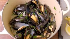 a pan filled with mussels and lemon slices on top of a wooden table