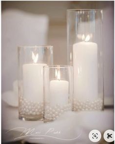 three white candles are sitting in glass vases with pearls on the bottom and sides