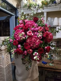 a vase filled with red and pink flowers sitting on top of a table next to a shelf