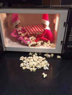 two elfs sitting in a microwave with popcorn spilled on the floor next to them