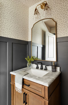 a bathroom vanity with a large mirror above it and a vase on the counter top