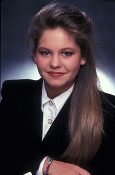 a woman with long hair wearing a black jacket and white shirt is smiling at the camera