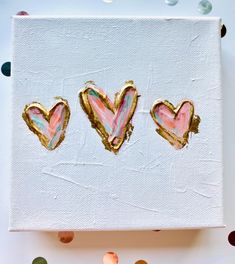 three hearts are painted on a canvas with gold foil and confetti around them