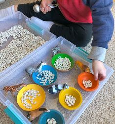 a little boy sitting on the floor playing with some food in plastic bowls and spoons