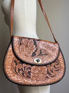 Vintage 70s hand tooled shoulder bag. Beautiful floral design. Stitched accents. Gold tone hardware. Substantial weight to this leather piece. Inside features dark brown leather lining. Three compartments total with one open pocket, one zippered and the main interior space. Additional measurement and condition information provided for your consideration. Maker: - Initialed CMJ on top flap. RAU hardware. Era: 1970s Material: Estimated to be genuine leather Lined: Yes - estimated to be leather Condition: Bag is in Very Good Vintage Condition (scale: Mint, Excellent, Very Good, Good, Fair, Poor.) The straps show normal wear and a few stitches and seams have un-raveled at the center of the strap - see photo. Tooled art remains intact and in good condition.  WIDTH: 10 3/4 inches at widest point Vintage Brown Hand Tooled Crossbody Shoulder Bag, Vintage Brown Hand-tooled Crossbody Shoulder Bag, Vintage Brown Hobo Bag With Leather Backing, Brown Hand-tooled Crossbody Shoulder Bag, Brown Hand Tooled Crossbody Shoulder Bag, Vintage Brown Hand Tooled Bag For Everyday Use, Retro Vintage Brown Hand Tooled Shoulder Bag, Retro Hand Tooled Satchel Shoulder Bag, Retro Hand-tooled Satchel Shoulder Bag