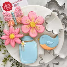 decorated cookies in the shape of flowers and butterflies on a plate with cookie cutters