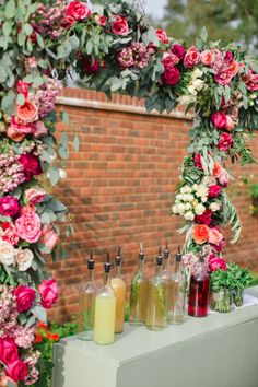 a table topped with drinks and flowers next to a brick wall covered in greenery