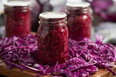 three jars filled with red cabbage on top of a wooden cutting board