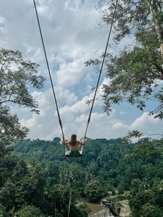 a woman is swinging from a rope in the air over a river and forest area