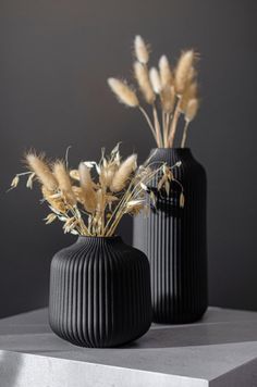 two black vases with dried plants in them