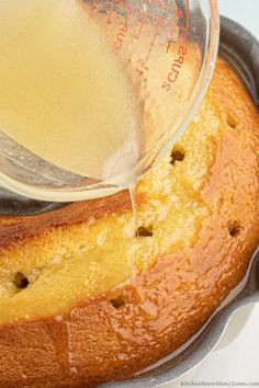 a person pouring liquid on top of a cake in a bundt pan with a measuring cup