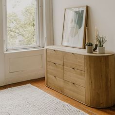 a wooden dresser sitting in front of a window next to a rug and potted plant