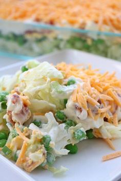 a white plate topped with a salad covered in cheese and peas next to a casserole dish