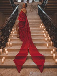 a woman in a red dress is sitting on some stairs with candles around her and looking up at the sky