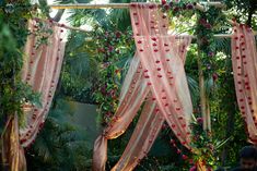 a man sitting in front of a canopy covered with pink and red flowers on it