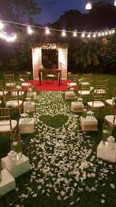 an outdoor ceremony set up with chairs and petals on the ground, surrounded by string lights