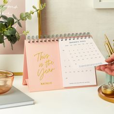 a desk calendar sitting on top of a table next to a cup and pen holder