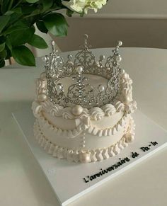 a white cake with a tiara on top sitting on a table next to flowers