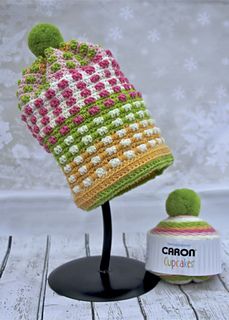 a crocheted hat is sitting on a stand next to a small cupcake