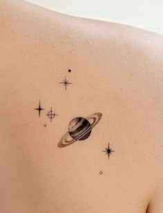 a woman's back with a small saturn tattoo on her left shoulder and stars in the background