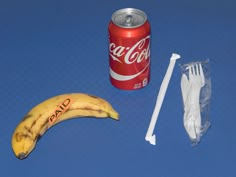 a can of coca - cola and a banana on a blue table with plastic straws