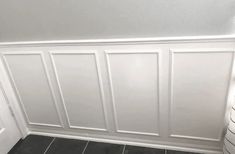 a bathroom with gray tile and white paneling on the wall next to a toilet