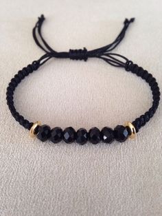 a black beaded bracelet with gold beads on a white cloth covered surface, close up