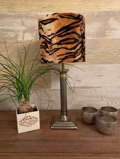 a lamp with a tiger print shade on it next to two cups and a plant