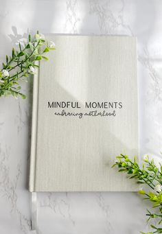 a book with the words mindful moments on it next to some flowers and leaves