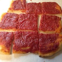 square pieces of pizza sitting on top of a piece of wax paper covered in sauce