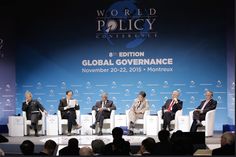 four men sitting on white chairs in front of a blue backdrop at the world policy conference