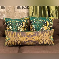 three decorative pillows sitting on top of a brown couch next to a green drapes