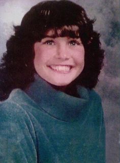 an old photo of a woman with long hair and wearing a green sweater smiling at the camera