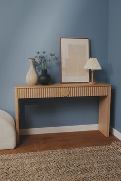 a wooden table with two vases and a lamp on it in a blue room